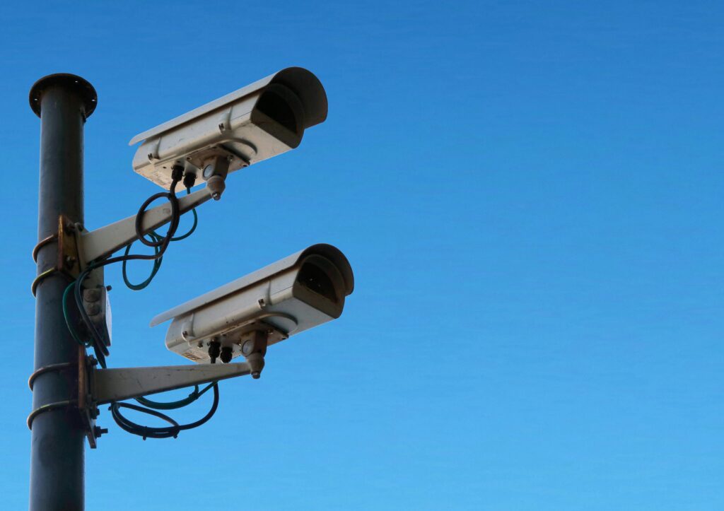 pexels-photo-5650141-5650141 Two security cameras mounted on a pole with a bright blue sky as the backdrop.